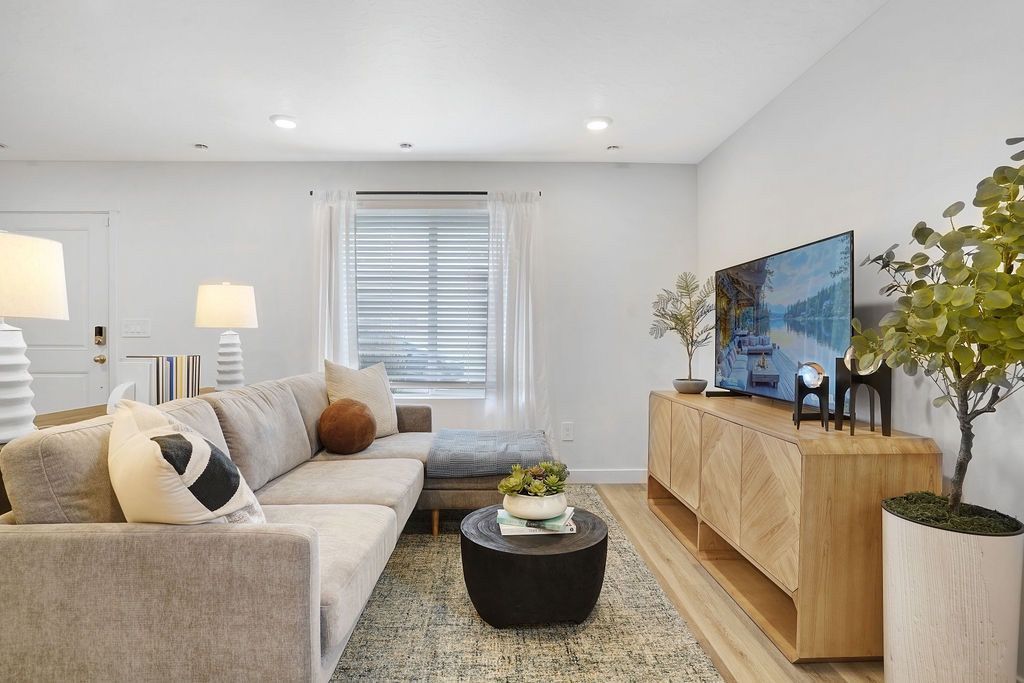 Bright living room in a modern apartment with a grey sectional sofa, window, and TV on a wooden console.
