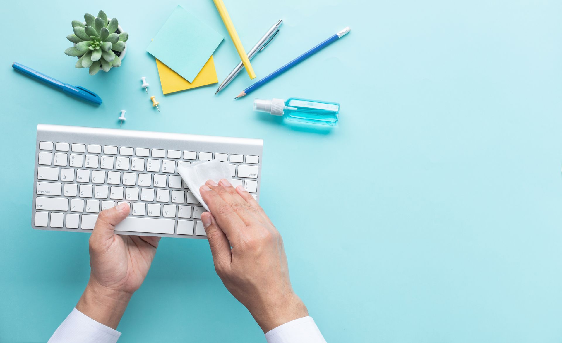 concept art, hands disinfect a keyboard on a desk with a teal background, showing how to clean desks and other germy office accessories