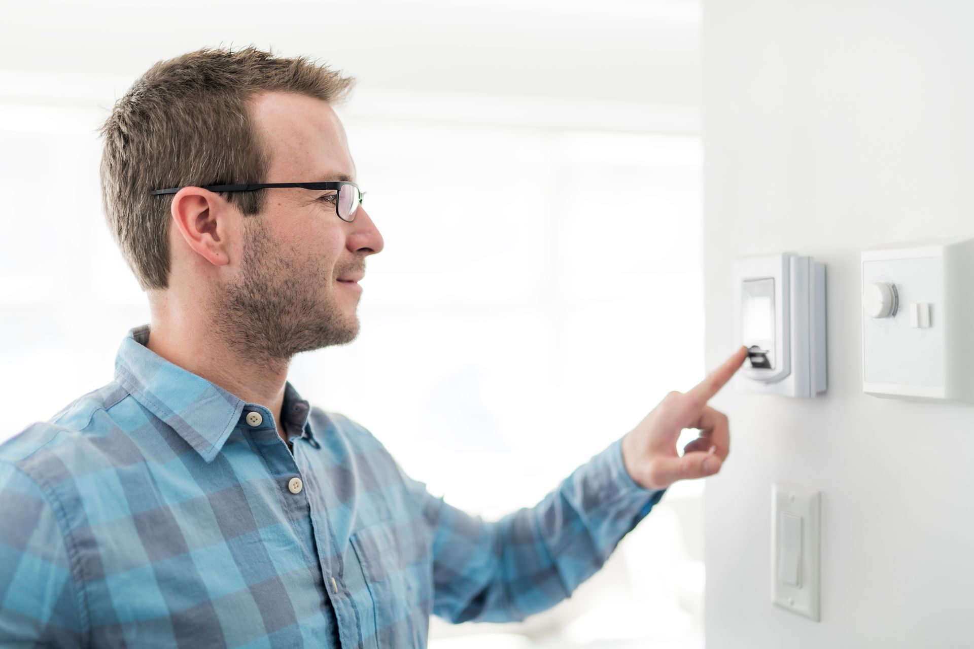 A man is adjusting a thermostat on a wall to help prevent his windows from fogging up