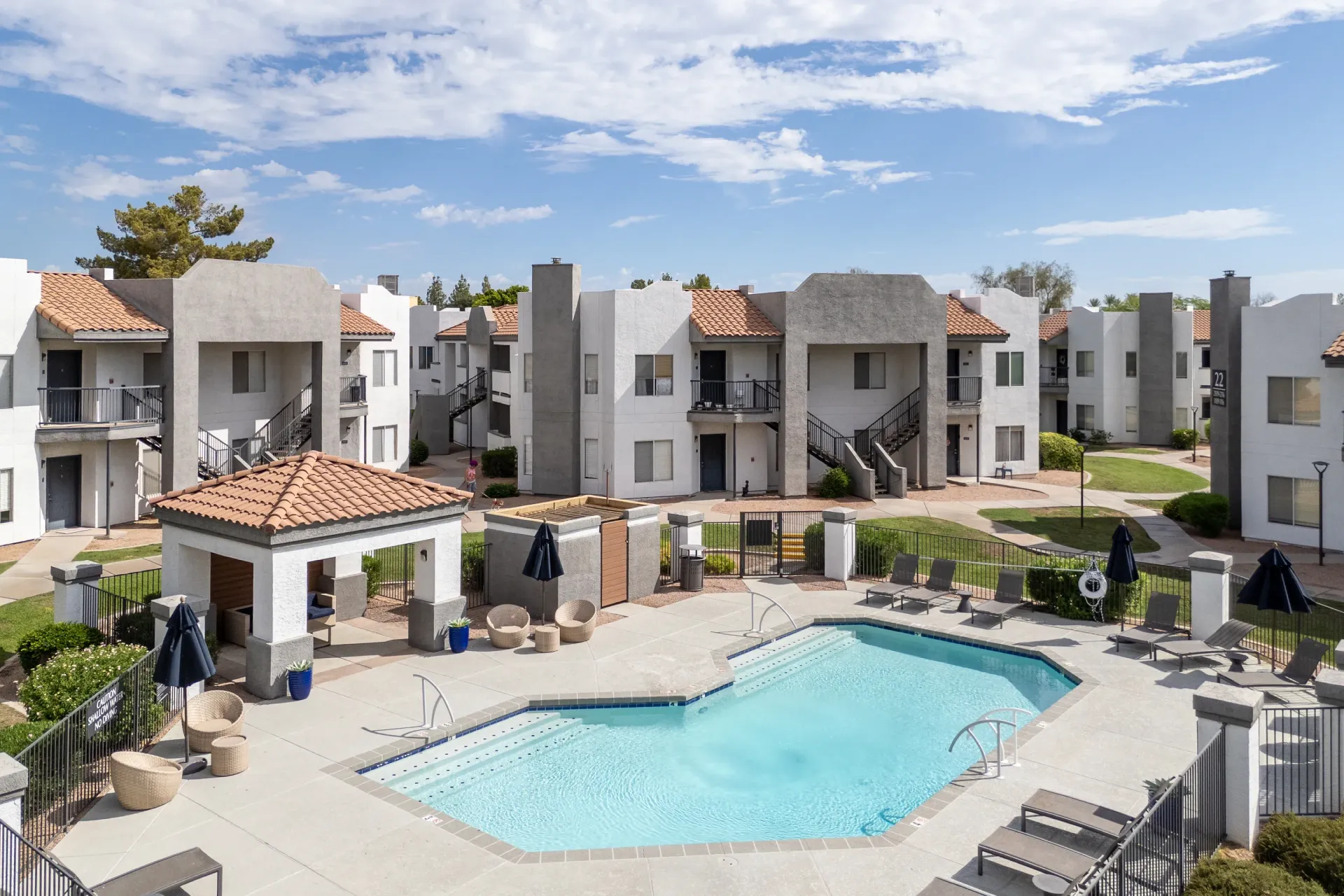 Apartment complex with a sparkling blue swimming pool and lounge chairs in the foreground.