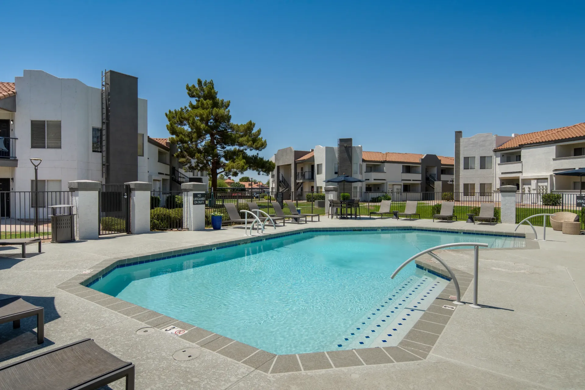 Swimming pool with lounge chairs and apartment buildings in the background.