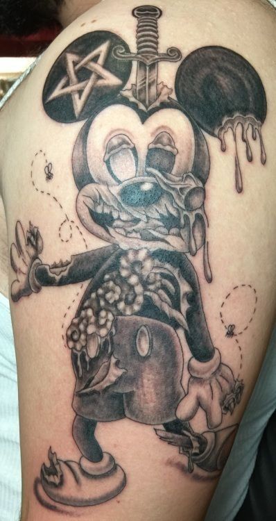 Tattoo of a decayed Mickey Mouse with a sword through the head, a star on one ear, and a zombie-like appearance.