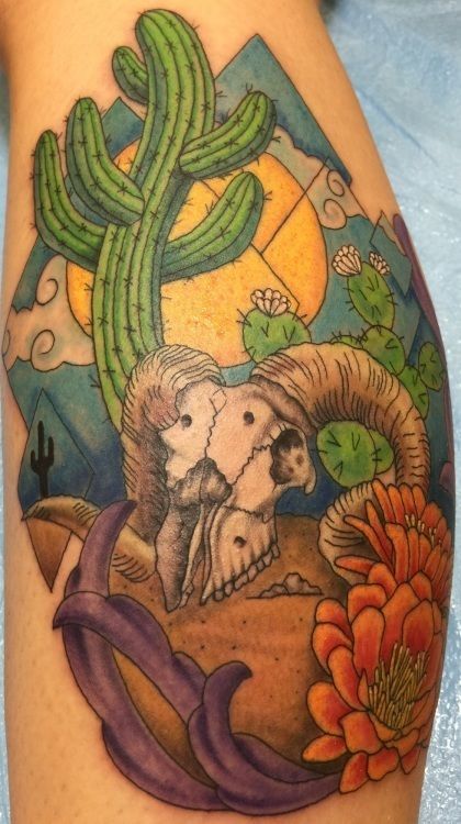 Tattoo of a desert scene with a ram skull, cacti, mountains, and orange flower.