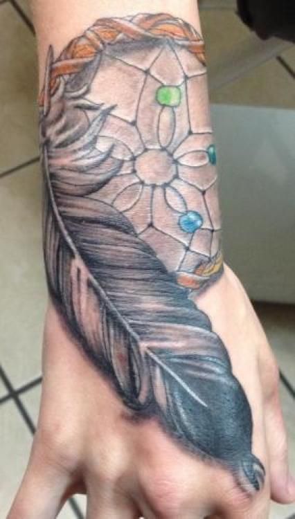 Dreamcatcher and feather tattoo on wrist, detailed gray and brown tones, with colorful beads.