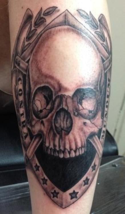 Tattoo of a skull within a shield and laurel leaves; text 