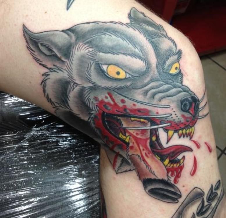Wolf head tattoo with open bloody mouth and yellow eyes.