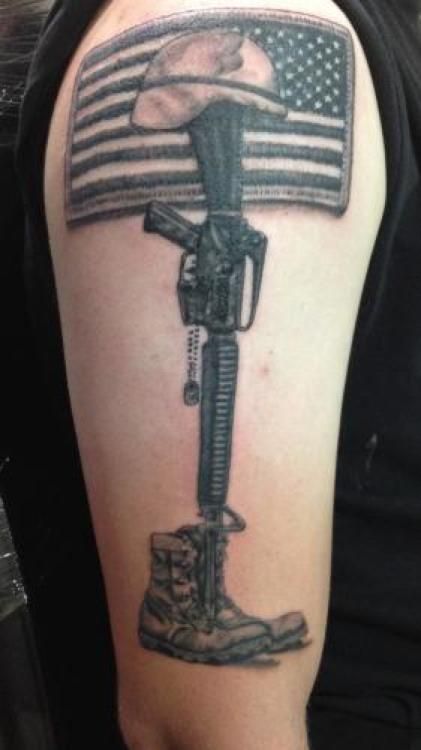 Tattoo of fallen soldier memorial: helmet on rifle, boots, and American flag.