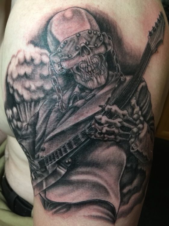 Tattoo of a skeletal figure wearing a metal helmet, playing a guitar, with a mushroom cloud in the background.