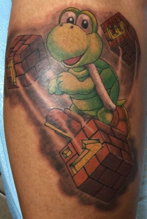 Cartoon Koopa Troopa character tattoo on skin, holding brick blocks, and smiling.