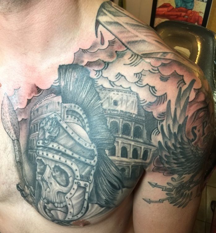 Tattoo of a skull in a Roman helmet and the Colosseum on a man's chest and shoulder, gray ink.