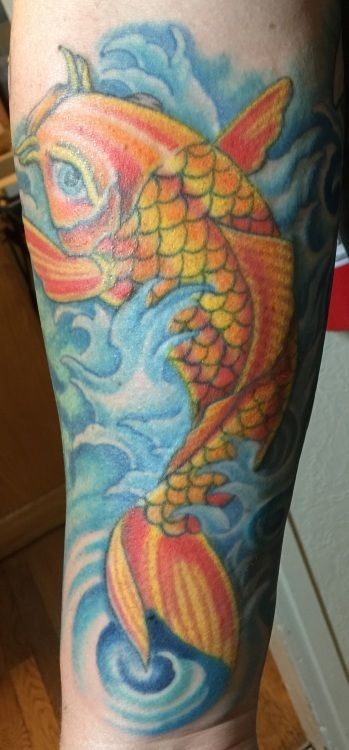 Koi fish tattoo on an arm, orange and yellow with blue waves in the background.