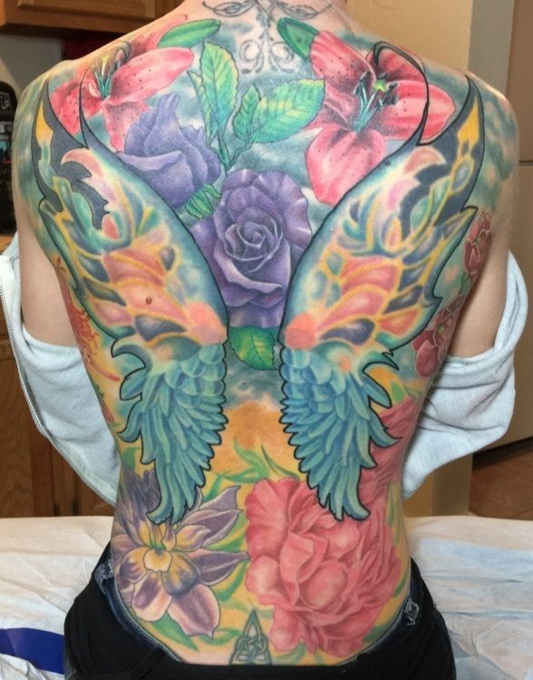Tattoo of colorful flowers and angel wings on a person's back.