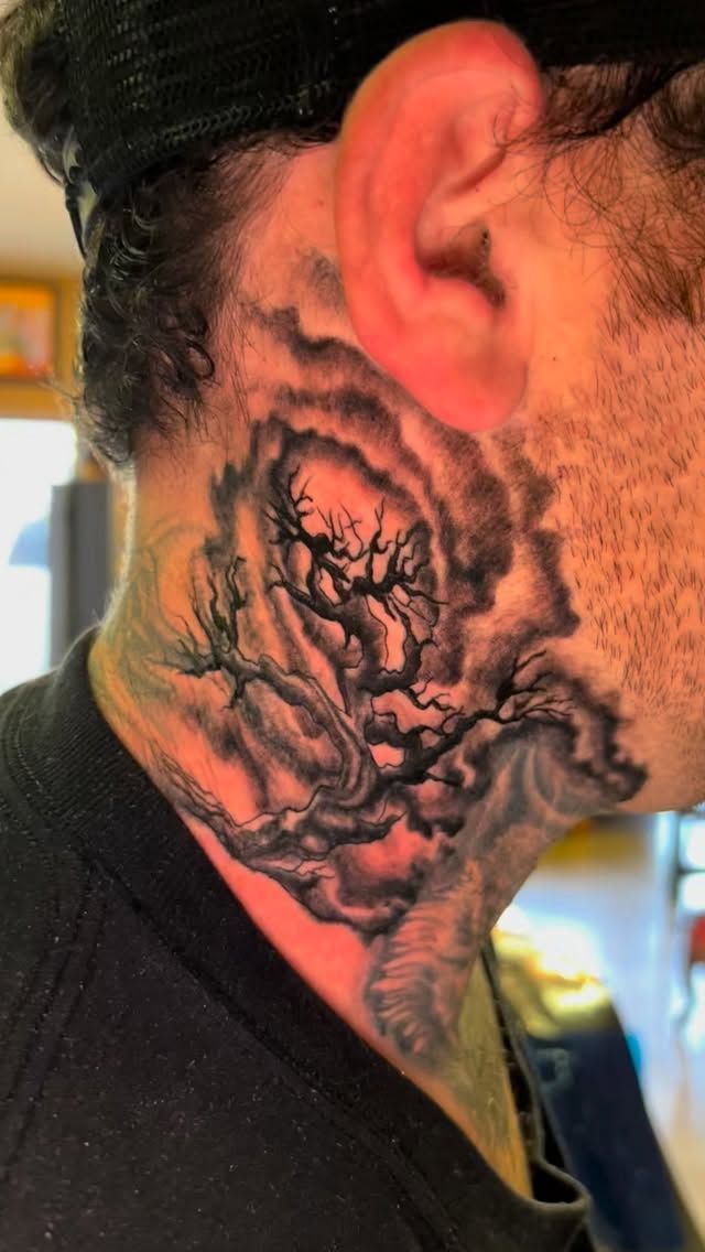 Man's neck tattoo depicts swirling dark clouds and bare tree branches.
