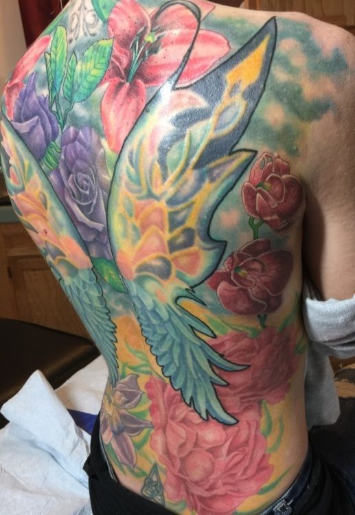 Tattoo of colorful floral design and stylized wings covering a person's back and side.