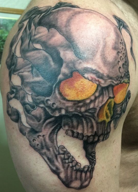 Skull tattoo with orange eyes on a shoulder.