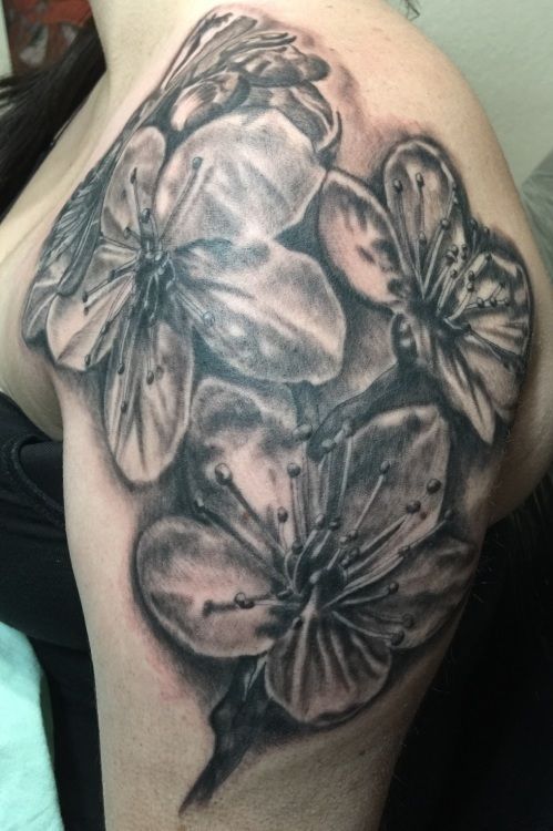 Black and white floral tattoo on a person's shoulder, featuring several detailed blossoms and stems.