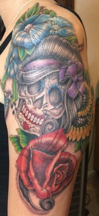 Tattoo of a sugar skull with flowers and a red rose on the arm.