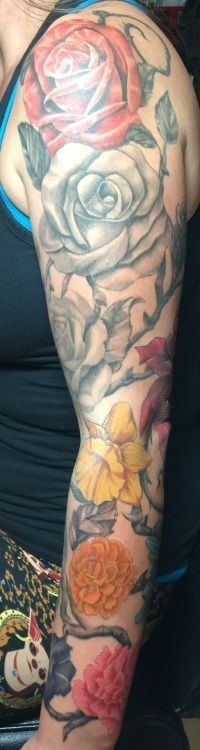 Tattoo of various colorful flowers, mainly roses, covering a person's upper arm.