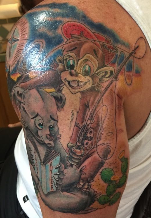 Tattoo of a monkey fishing with a sad bear reading a book; blue and yellow background, desert scene.