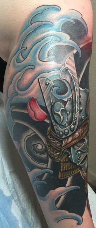 Arm tattoo of samurai armor with ocean waves, red petal, and dark background.