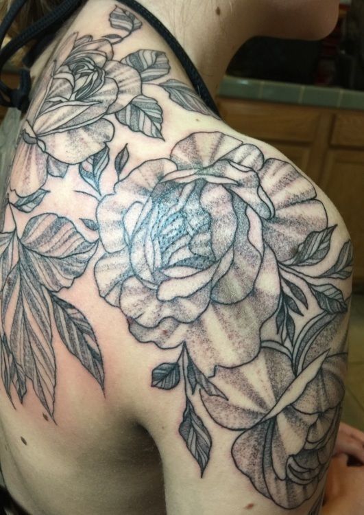 Tattoo of large roses and leaves in black ink on a shoulder and arm.