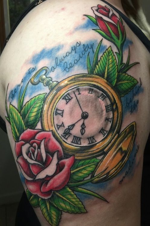 Tattoo on shoulder: gold pocket watch with roses and green leaves, surrounded by blue sky and the words 
