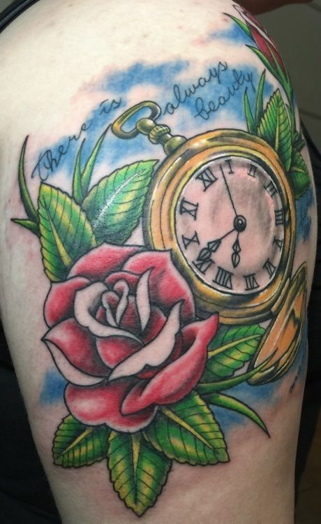 Tattoo of a rose, pocket watch, and foliage against a blue sky. Text reads 