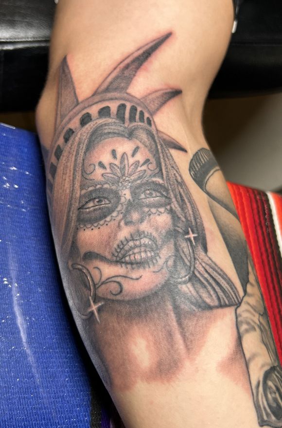 Tattoo of the Statue of Liberty face designed in a sugar skull style, on an arm.