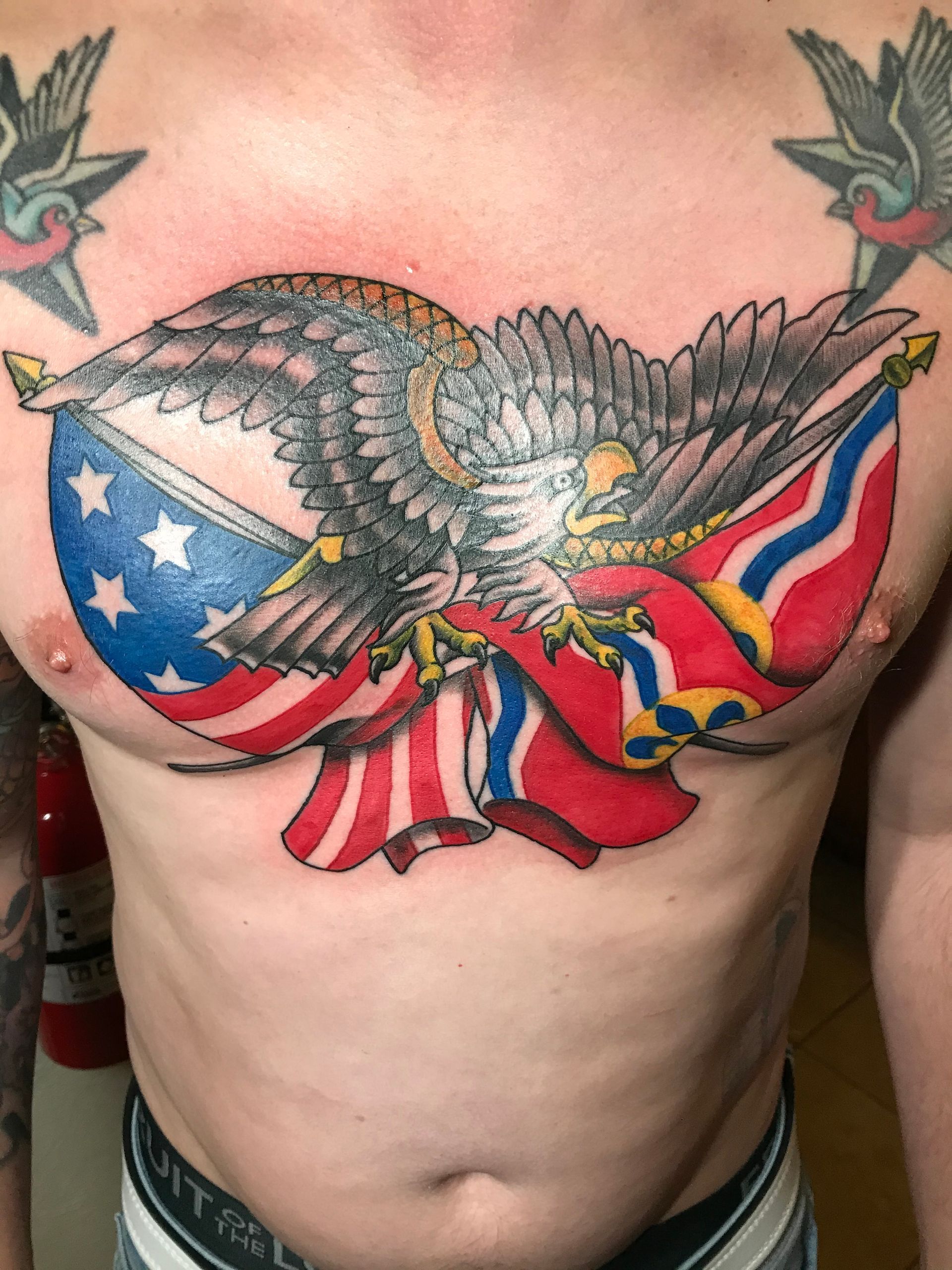 Tattoo of an eagle with outstretched wings clutching flags (U.S. and Confederate) on a person's chest.