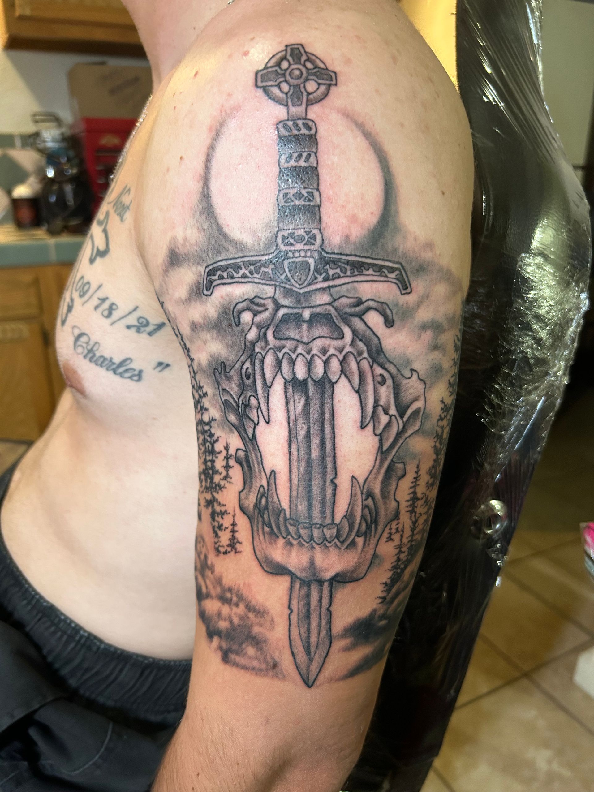 Tattoo of a sword piercing a skull on a person's upper arm.