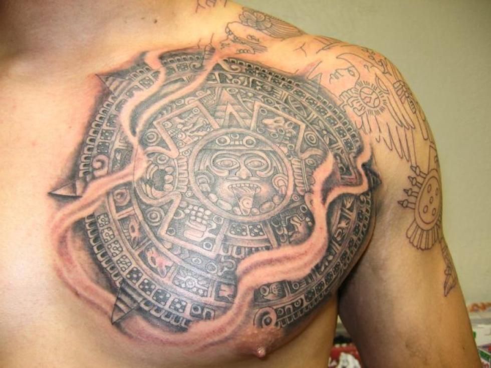 Tattoo of Aztec calendar on a person's chest. Gray shading with a torn skin effect.