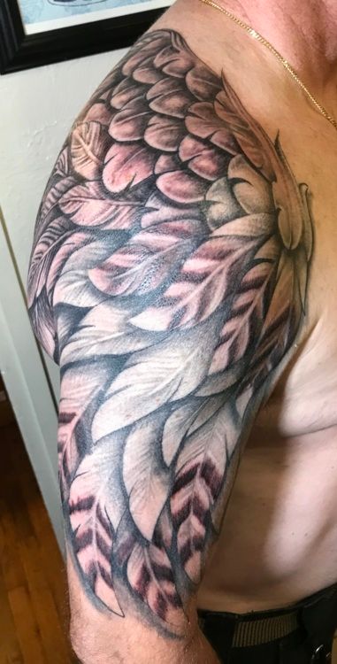 Tattoo of a wing in grayscale, covering a man's upper arm. Feathers are detailed, with shading and color variations.