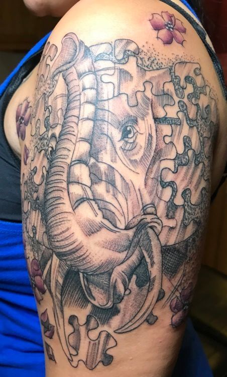 Tattoo of an elephant's head formed by puzzle pieces, shaded in black and gray, with pink flowers.