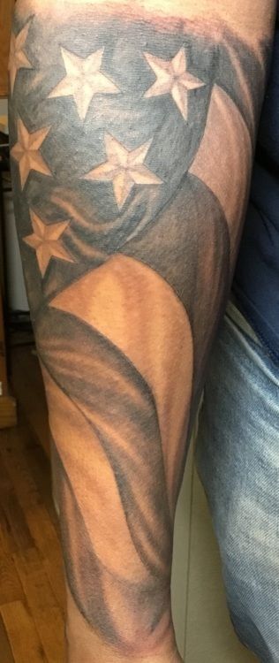 Tattoo of a black and white American flag waving on a person's arm.
