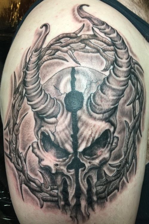 Skull tattoo with horns and vine-like border. Black and gray shading on upper arm.