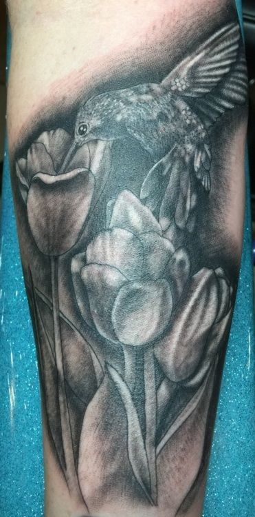 Black and white tattoo of a hummingbird hovering near tulips.