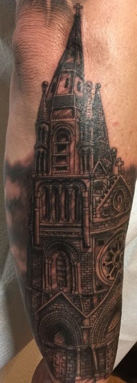 Black and gray detailed tattoo of a gothic cathedral on a person's forearm.