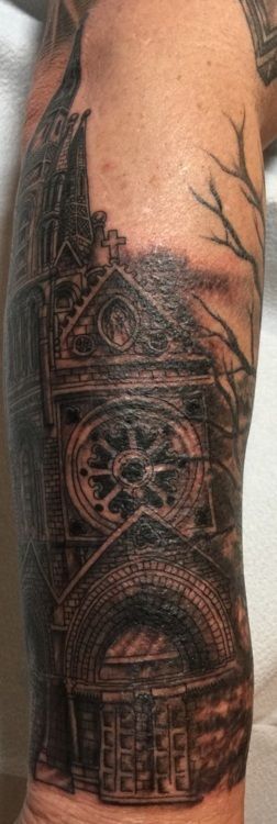 Tattoo on arm, detailed depiction of a gothic church facade, featuring a rose window.