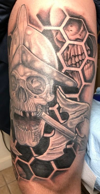 Tattoo of a skull in a helmet with an ax, set within a honeycomb pattern, on a person's leg.