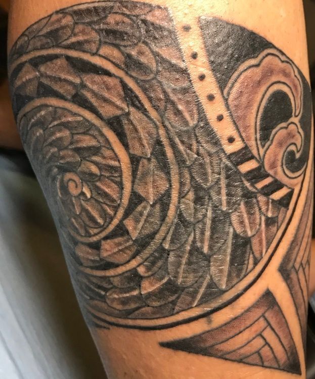 Black and gray tribal tattoo on arm featuring spiral, wave, and geometric patterns.