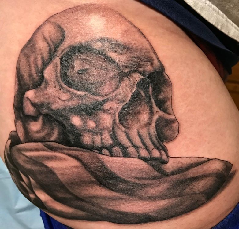 Black and gray skull tattoo on skin, resting on a flowing cloth.