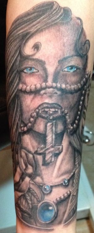 Tattoo of a veiled woman, pearls, a cross, and an ornate cuff with a blue gem. Black and white.