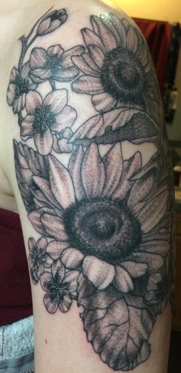 Tattoo of sunflowers and small flowers on a person's arm. The tattoo is in black and gray ink.
