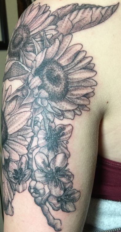 Black and white floral tattoo on arm; sunflowers, leaves, and smaller flowers.