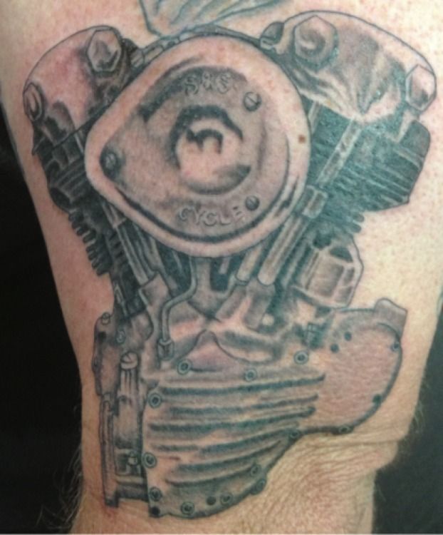 Black and gray tattoo of a motorcycle engine on a person's skin.