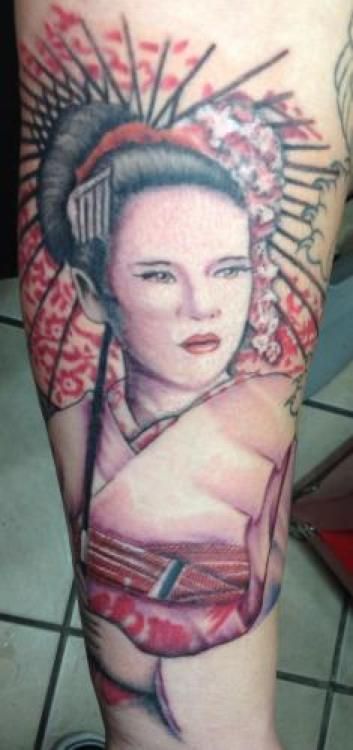 Tattoo of a geisha with black hair, red lips, and a floral and parasol design in red and black ink.