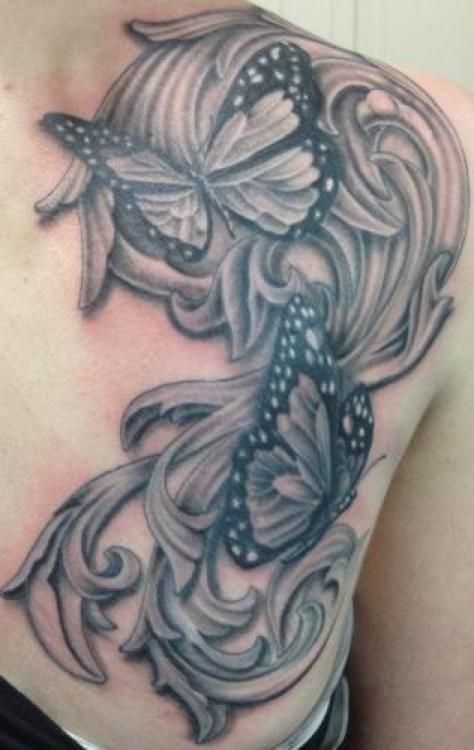 Black and white tattoo of butterflies and ornate scrolling design on shoulder.