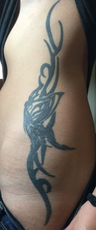 Tattoo in black ink, tribal design down side of torso.