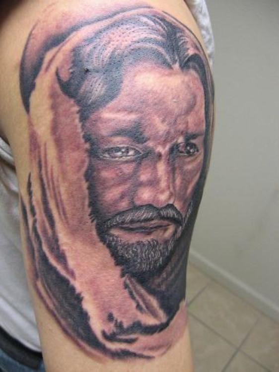 Tattoo on arm of a man with a beard, in a head covering; grayscale portrait.