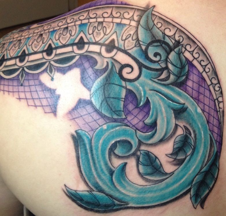 Blue and purple ornate tattoo design on a back, featuring swirling shapes, leaves, and intricate border details.